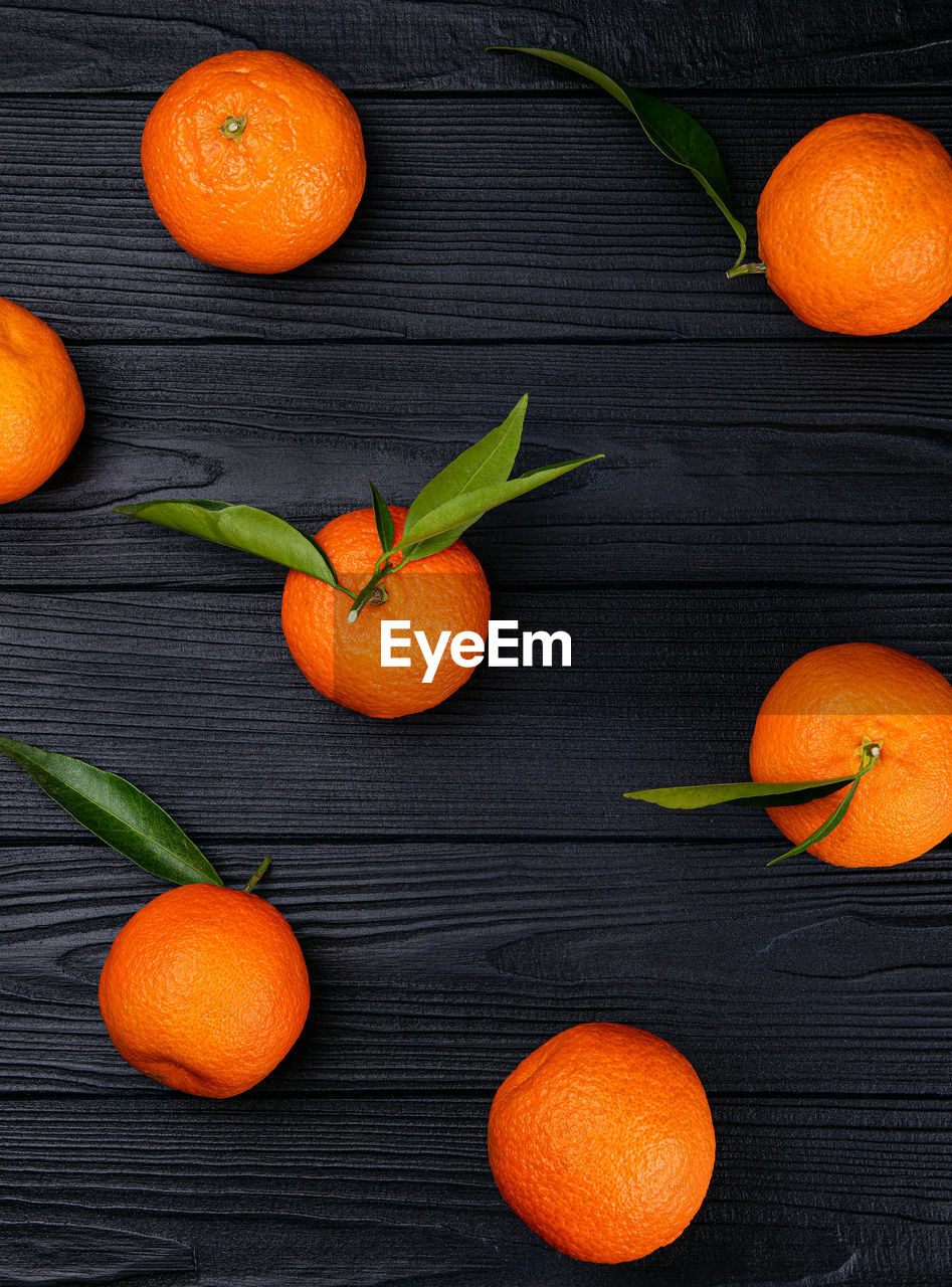 Top view of whole ripe fresh citrus fruits tangerines with green leaves on black background 