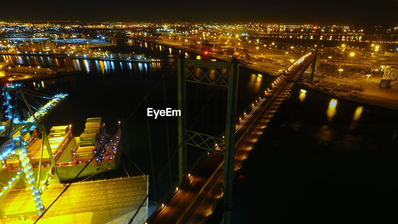 Illuminated bridge over river in city at night