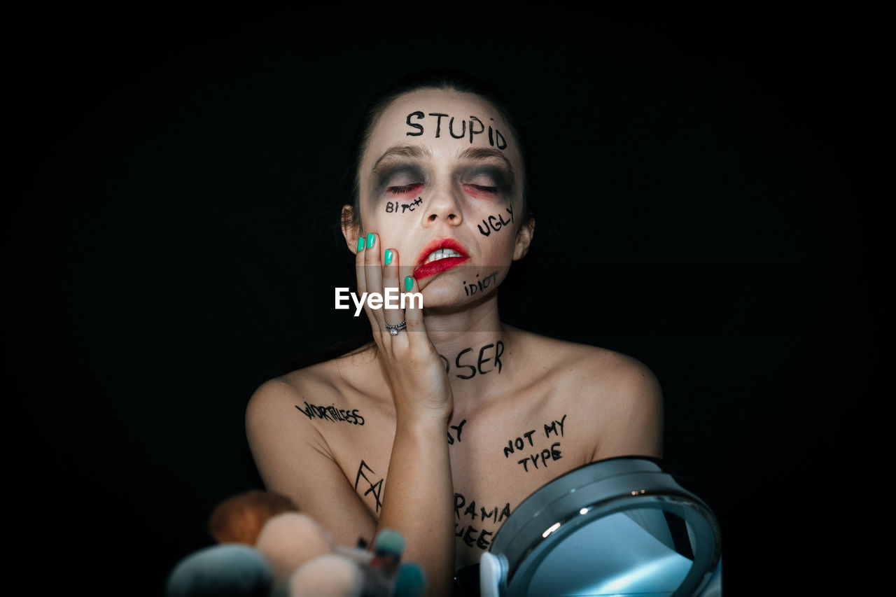 Eyes closed woman with text on body sitting against black background