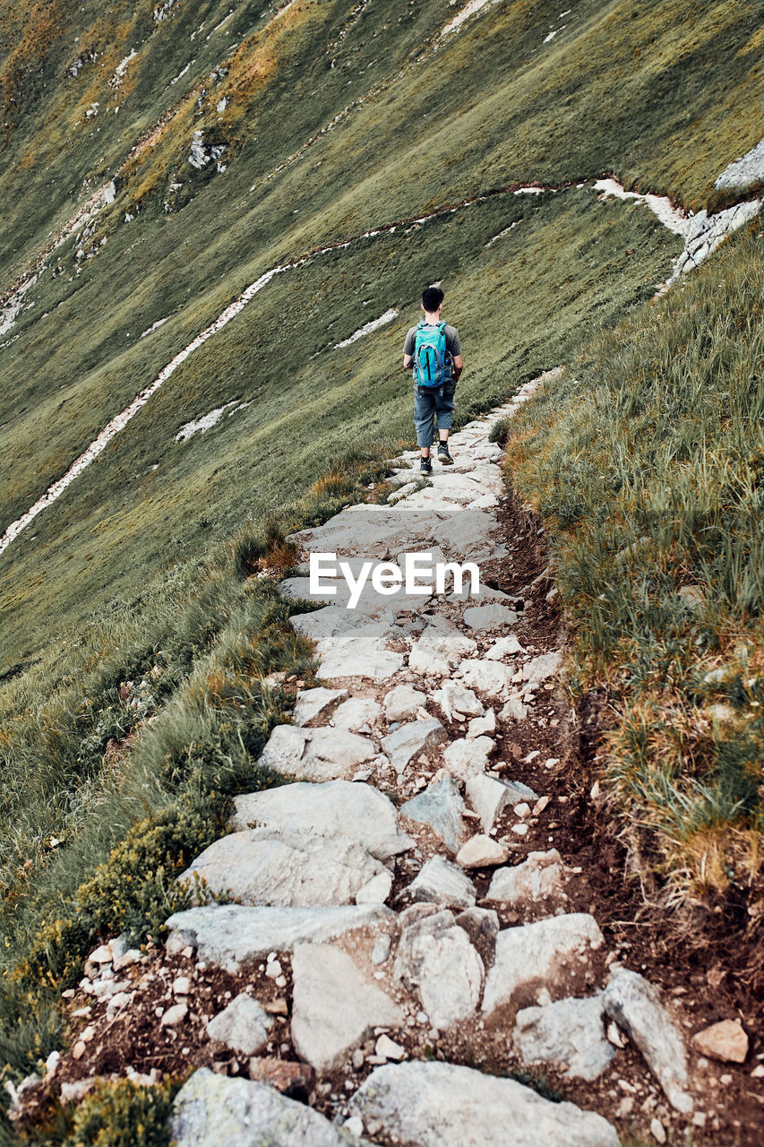 Young man with backpack hiking in a mountains, actively spending summer vacation