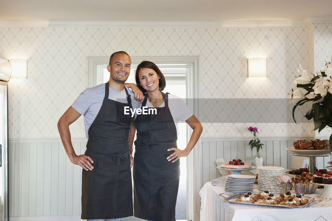 Portrait of smiling owners standing by dessert decorated table at cafe