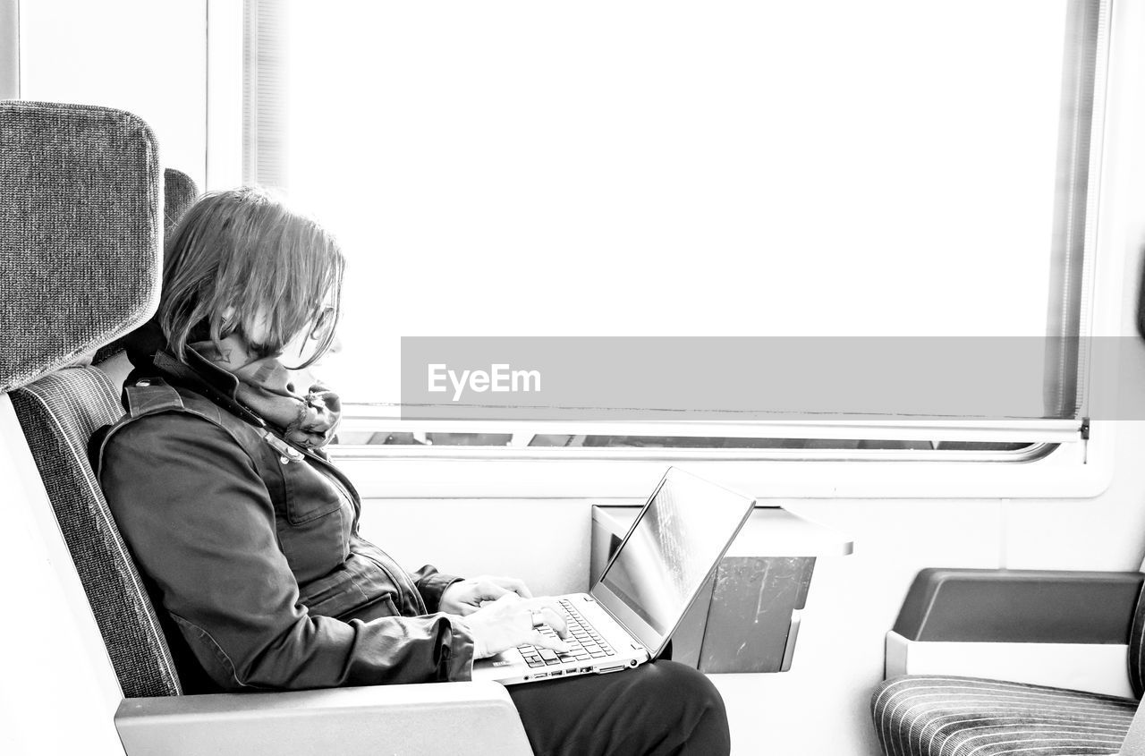 Side view of woman using laptop in train