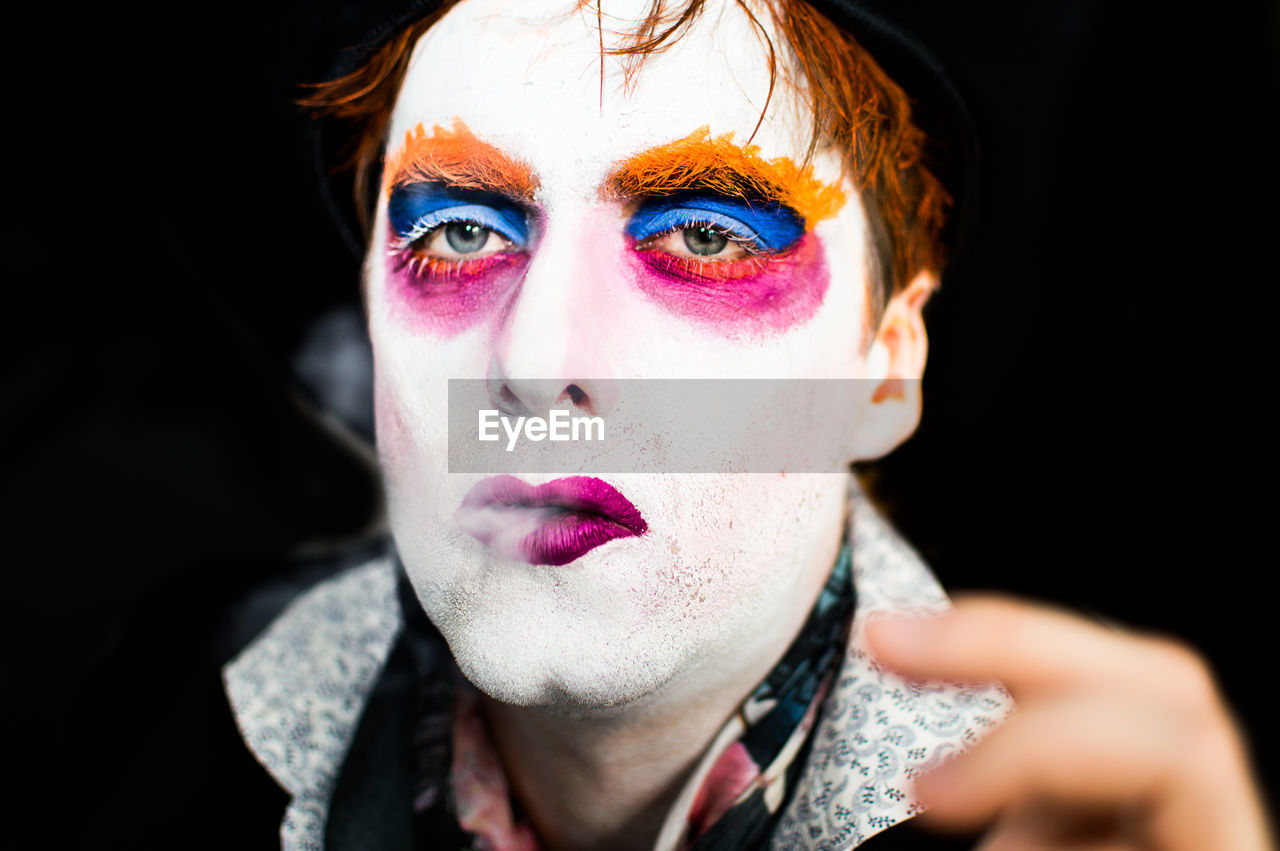 Close-up portrait of man with face paint smoking against black background