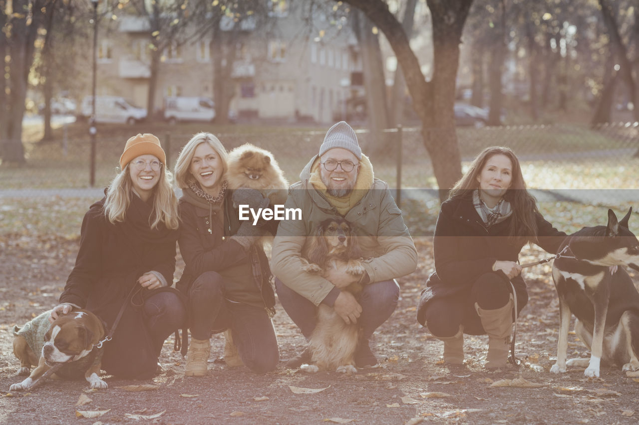 Portrait of happy man and women crouching with dogs at park during autumn