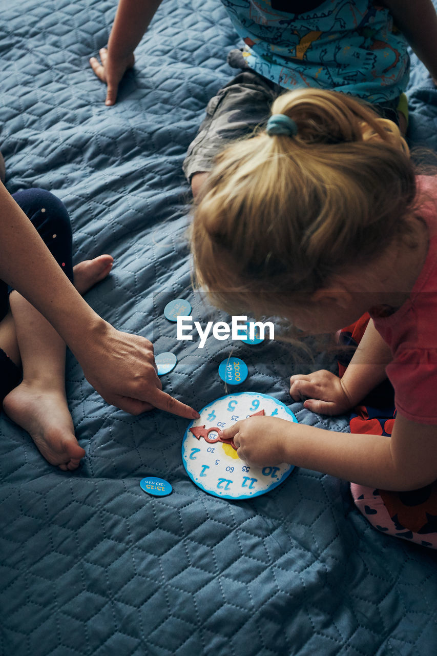 High angle view of people sitting by toy clock on bed