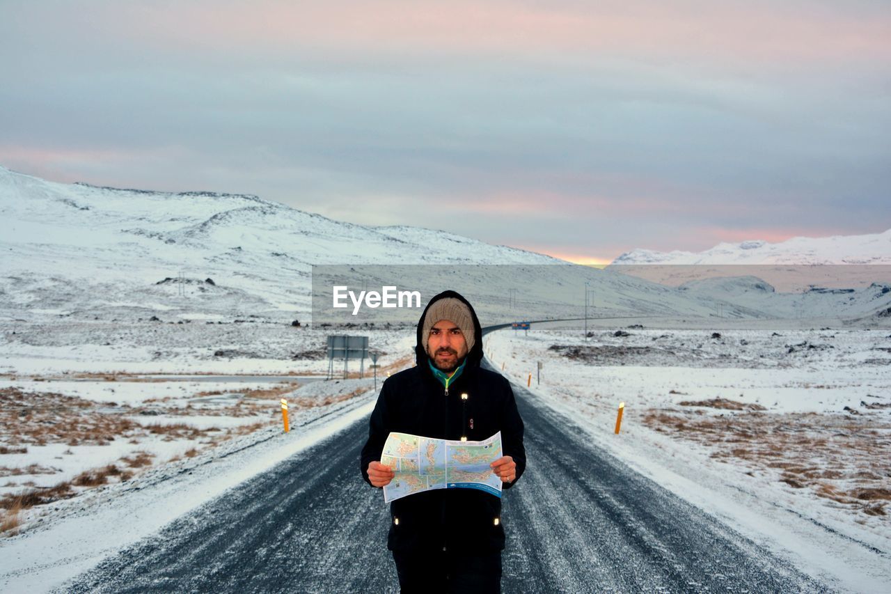 Portrait of man holding map while standing on snow covered road