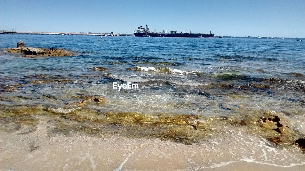 SEA WAVES SPLASHING ON BEACH AGAINST CLEAR SKY