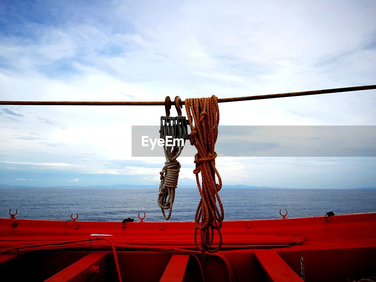 Rope hanging on railing by sea against sky