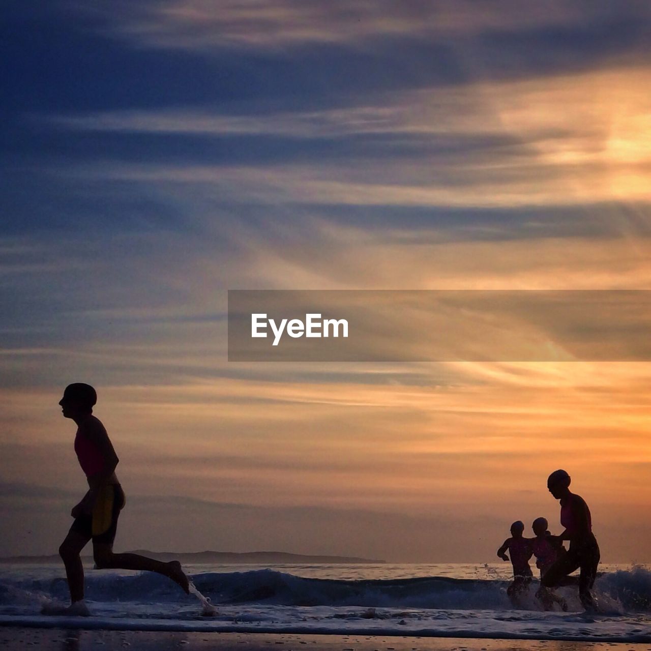 Low angle view of friends running on beach against cloudy sky at dusk