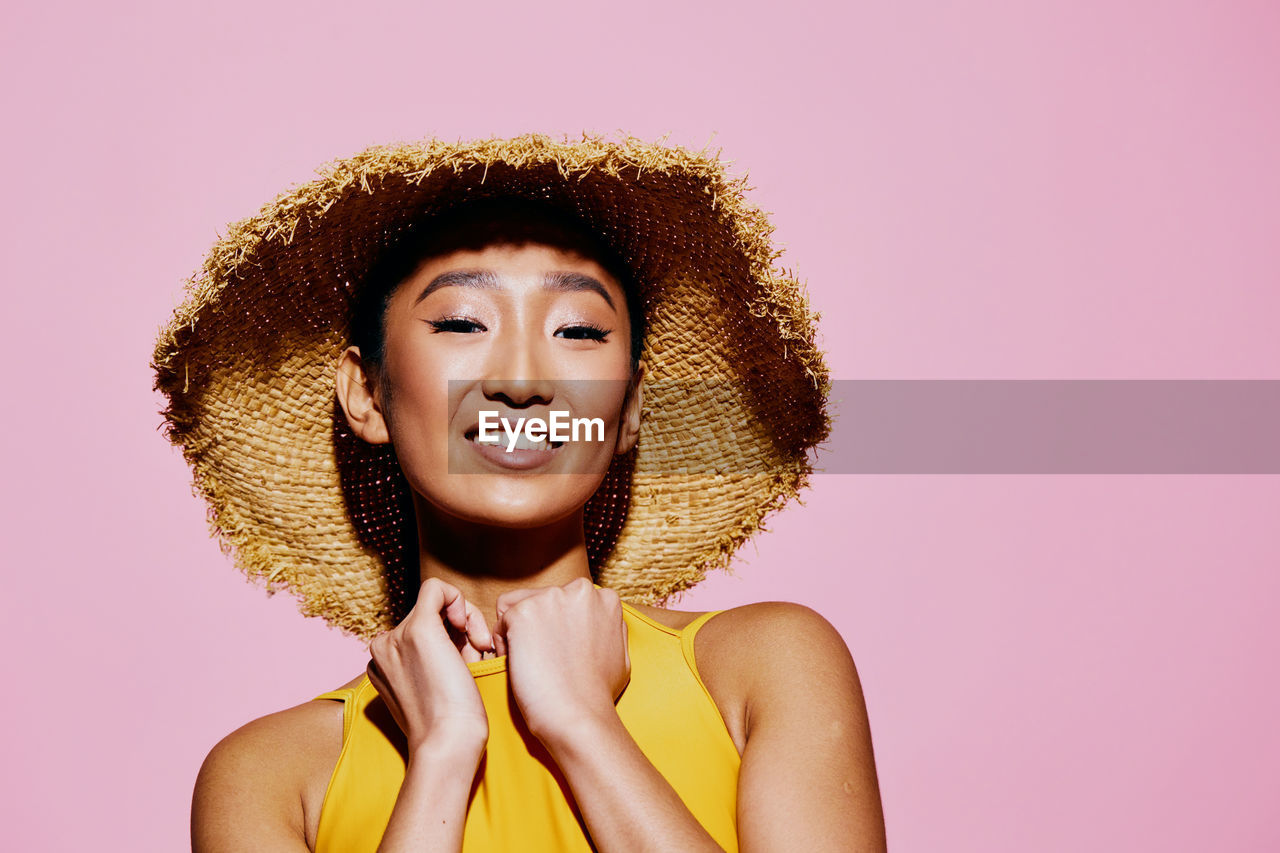 portrait of beautiful young woman wearing hat against pink background