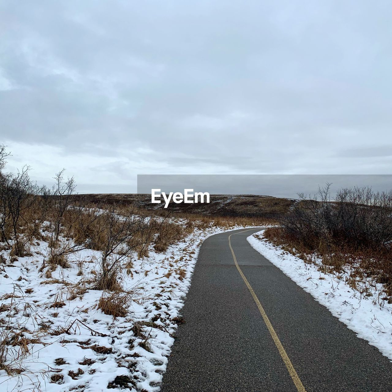 Surface level of road on snow covered field against sky