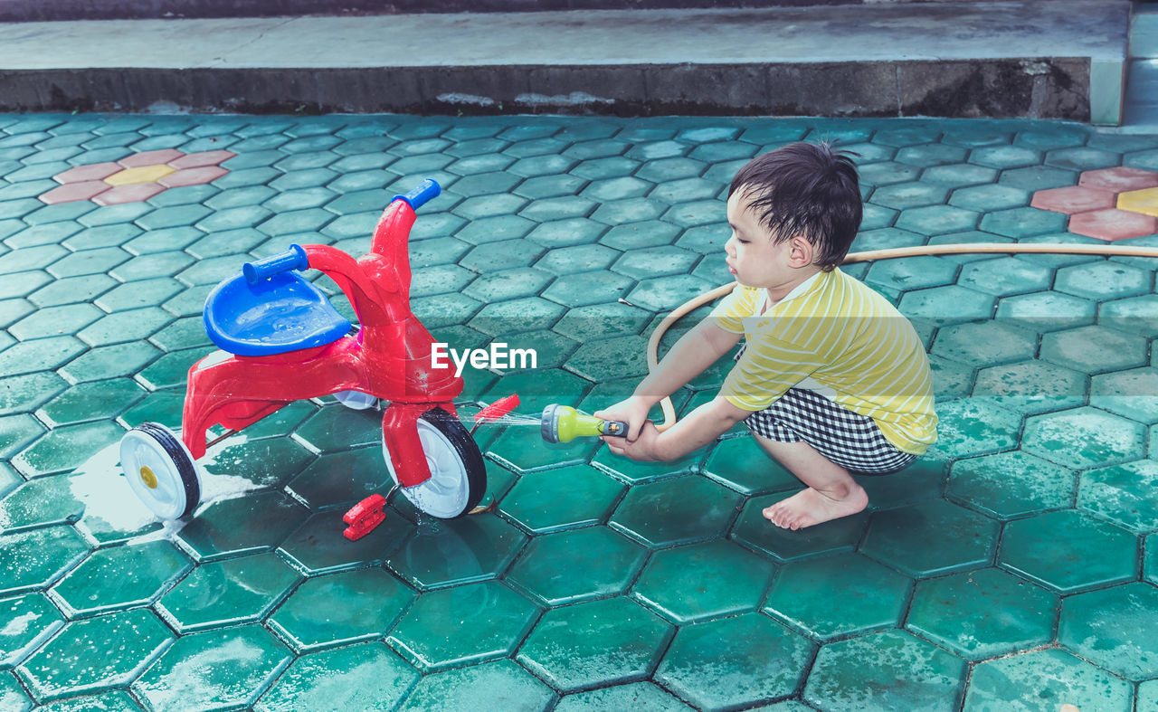 High angle view of boy washing tricycle outdoors