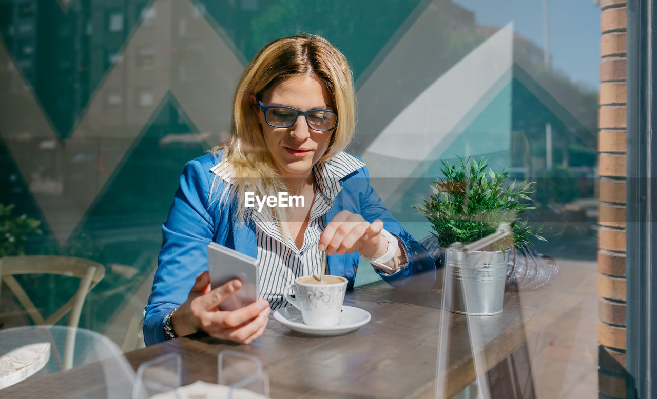 Young woman using mobile phone seen through glass at cafe