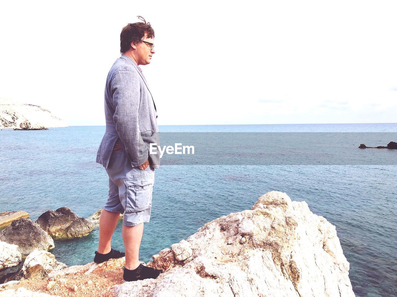 Side view of mature man looking at sea while standing on rock against clear sky