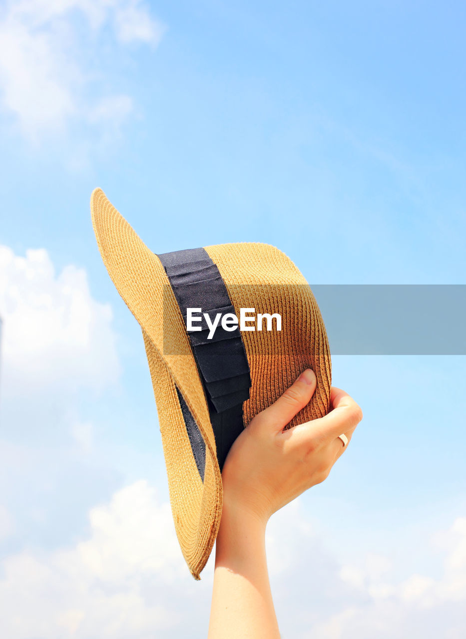 Low angle view of person holding hat against sky