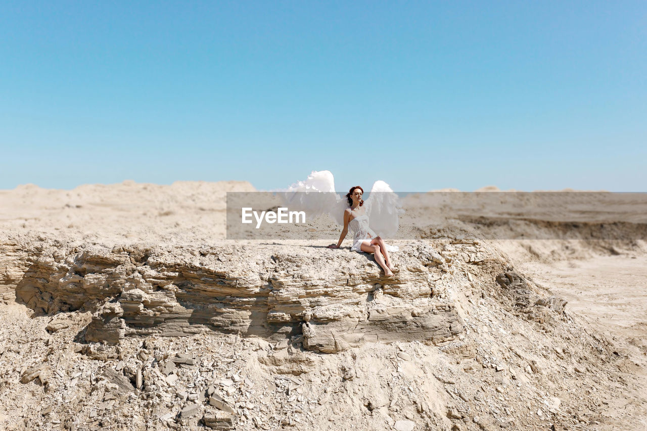 Side view of woman with white wings on land against sky