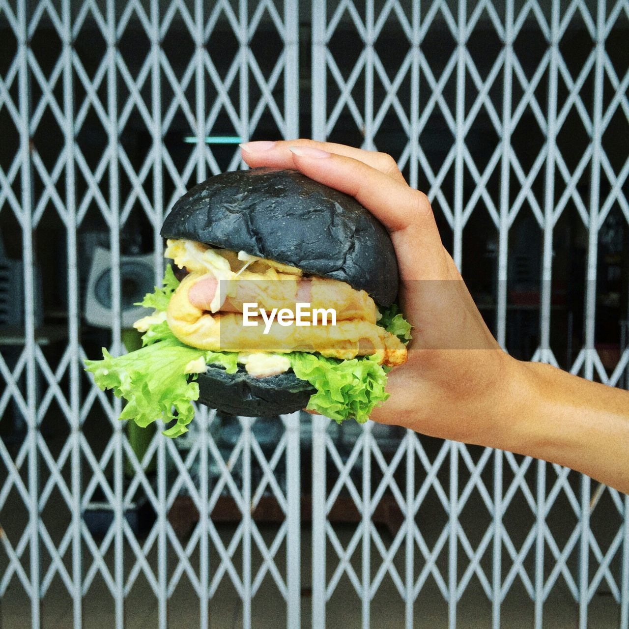 Cropped image of hand holding black burger against gate