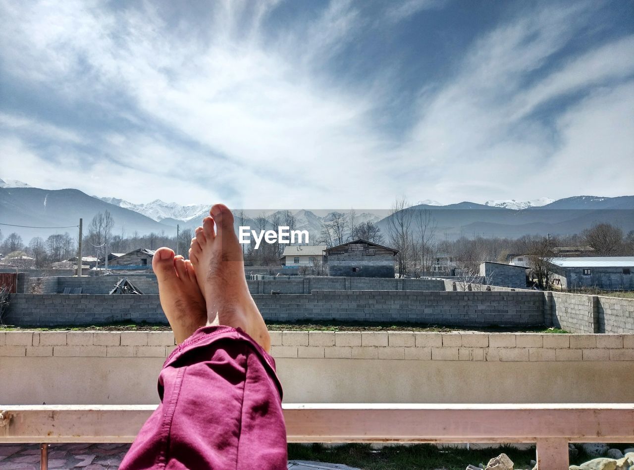 Low section of man with feet up of railing against sky