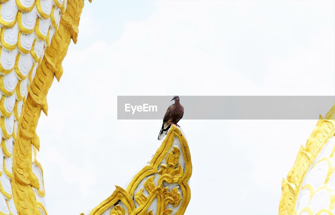 Low angleview of bird perching on sculpture against sky