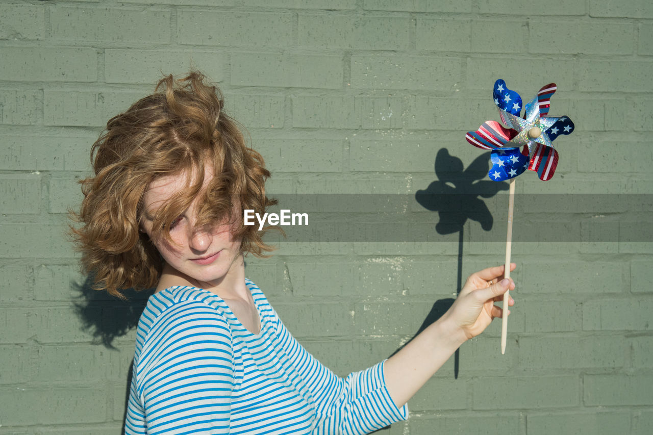 Woman with tousled hair holding american flag pinwheel toy by green wall
