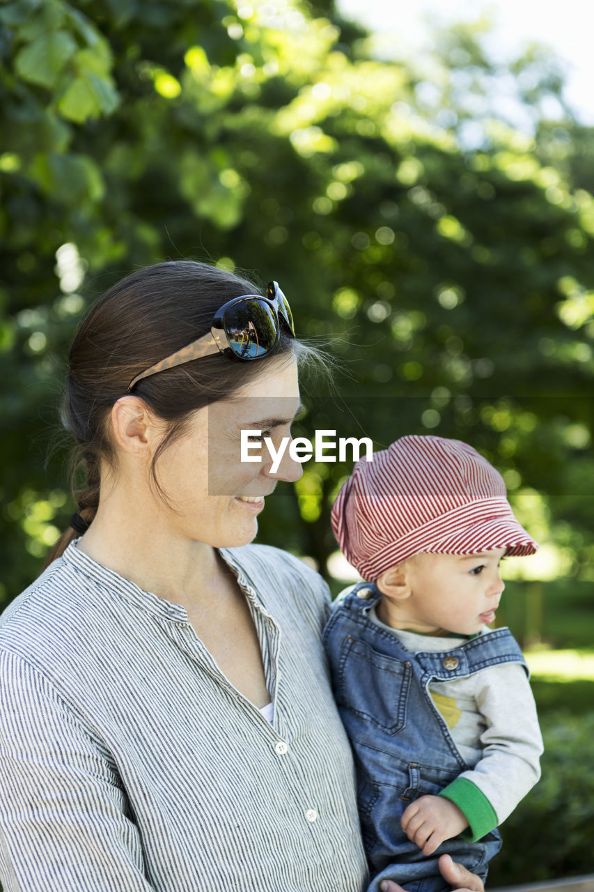 Smiling mother looking away while carrying baby girl outdoors