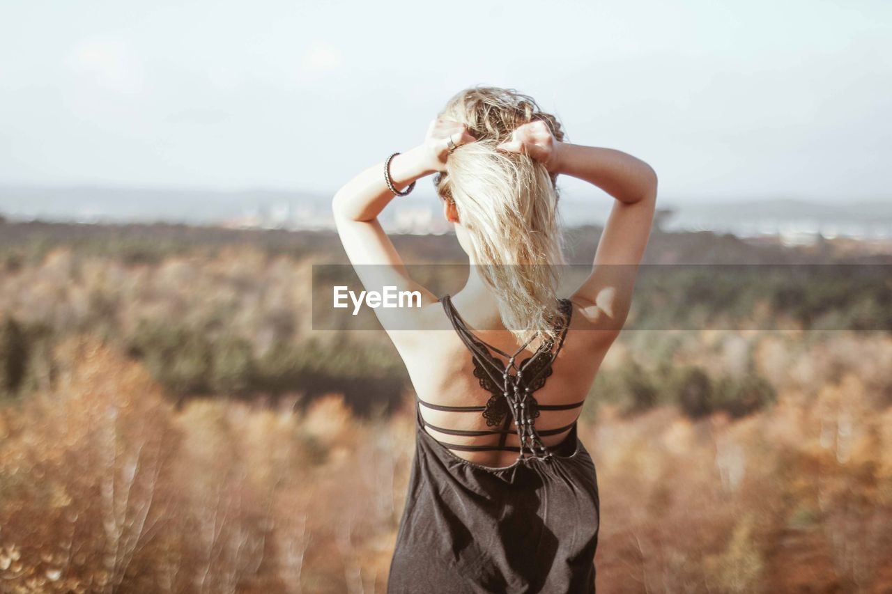 Rear view of woman with hands in hair standing on field