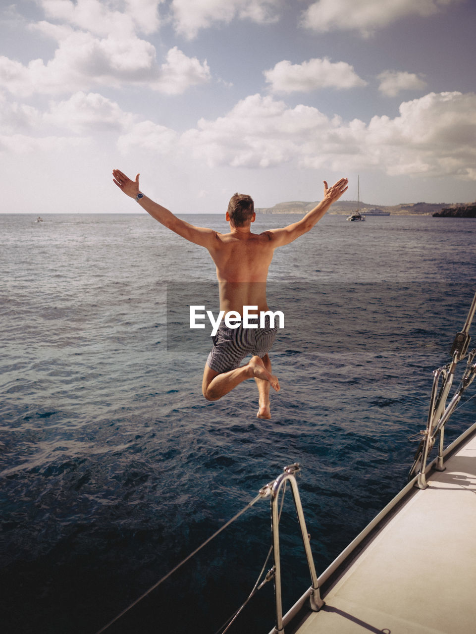 Full length rear view of man jumping from boat into sea on sunny day