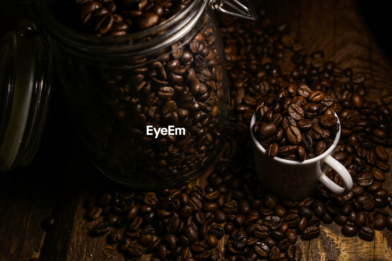 Roasted coffee beans in glass jar and cup on table