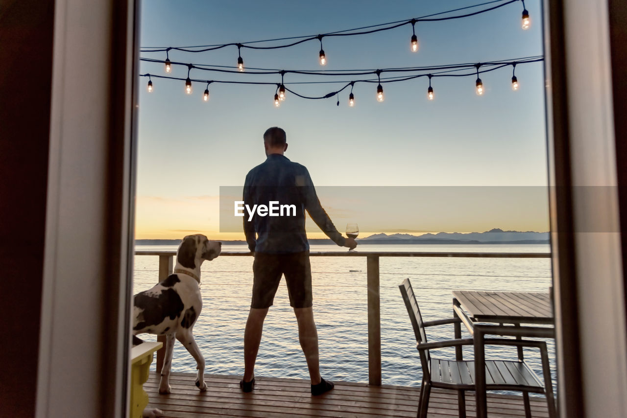 Man with dog standing in boat deck over sea against sky