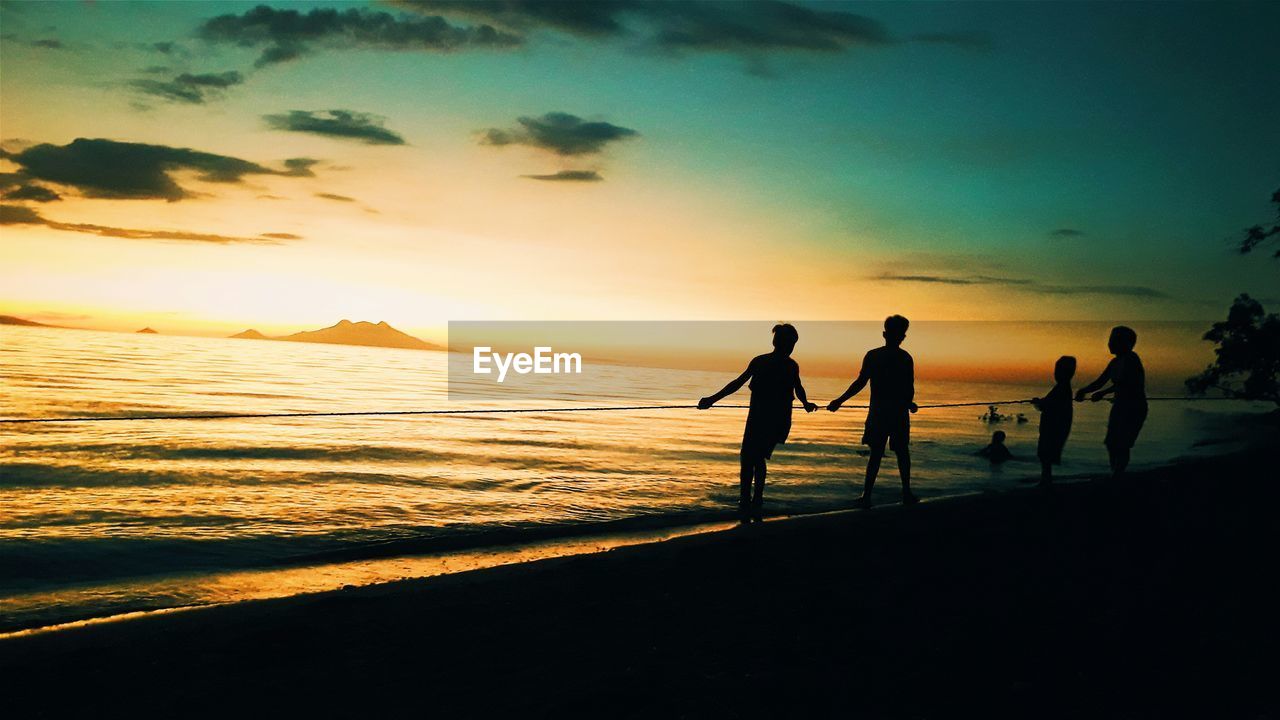 SILHOUETTE PEOPLE ON BEACH AGAINST SKY DURING SUNSET