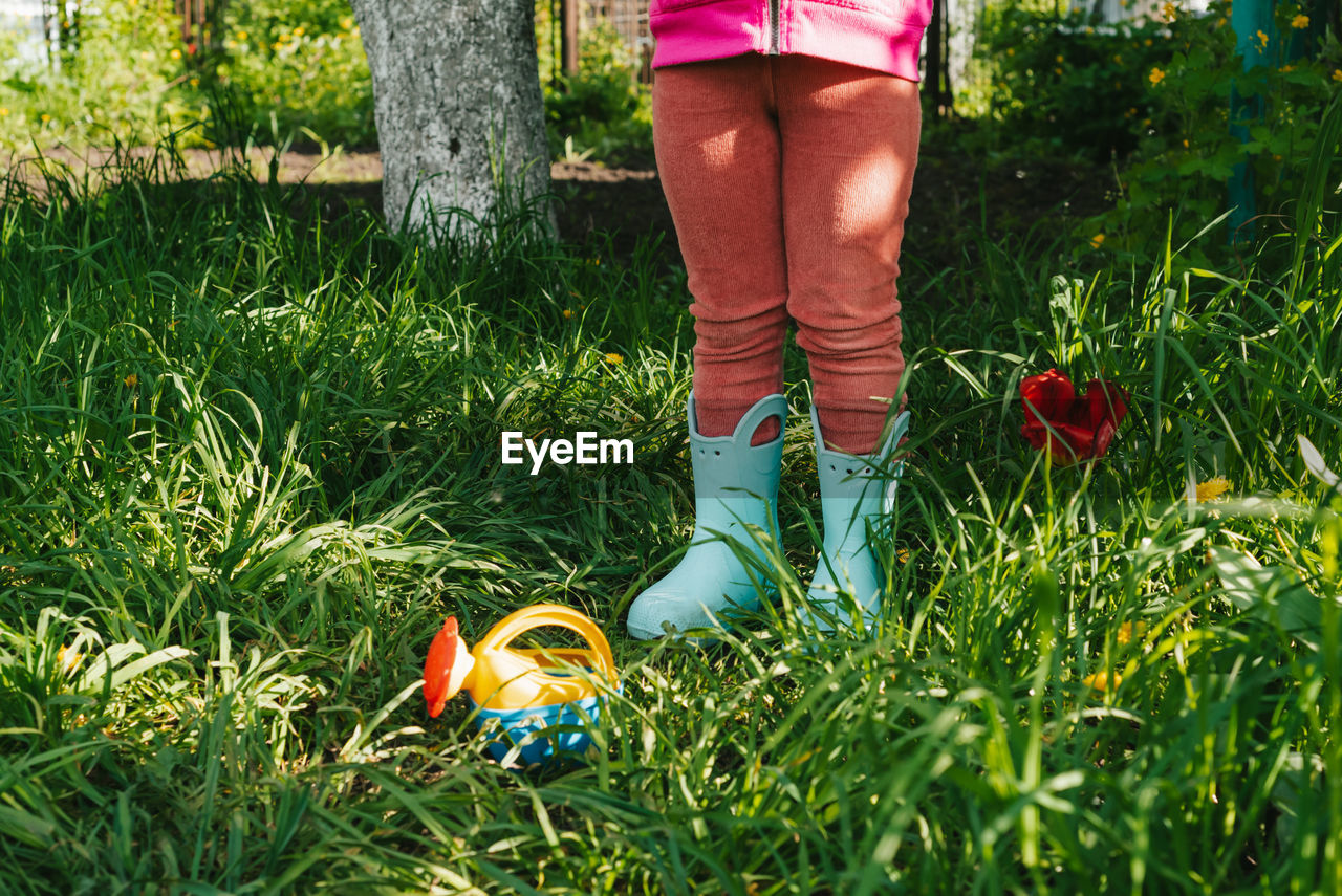 Child in rubber boots stands in the garden near a small watering can. part of the human body. 