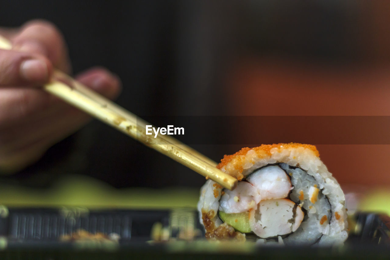 Close-up of a hand holding sushi with chopsticks