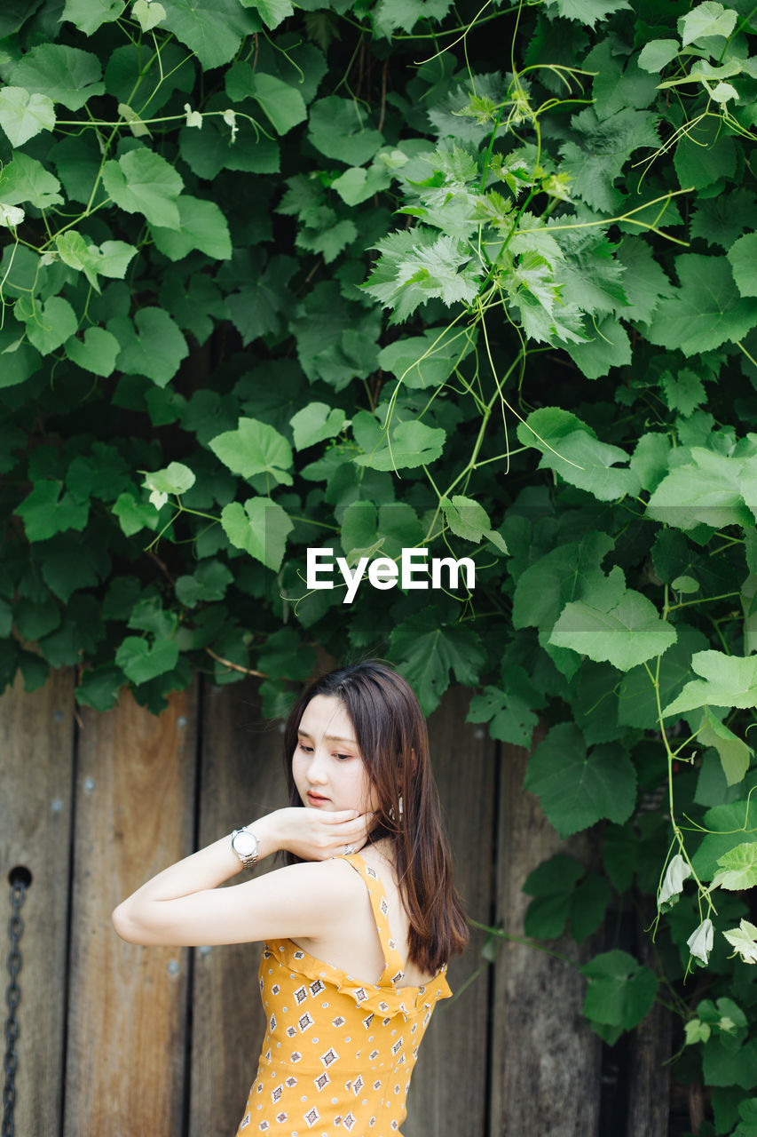 Beautiful woman standing by wooden wall against tree