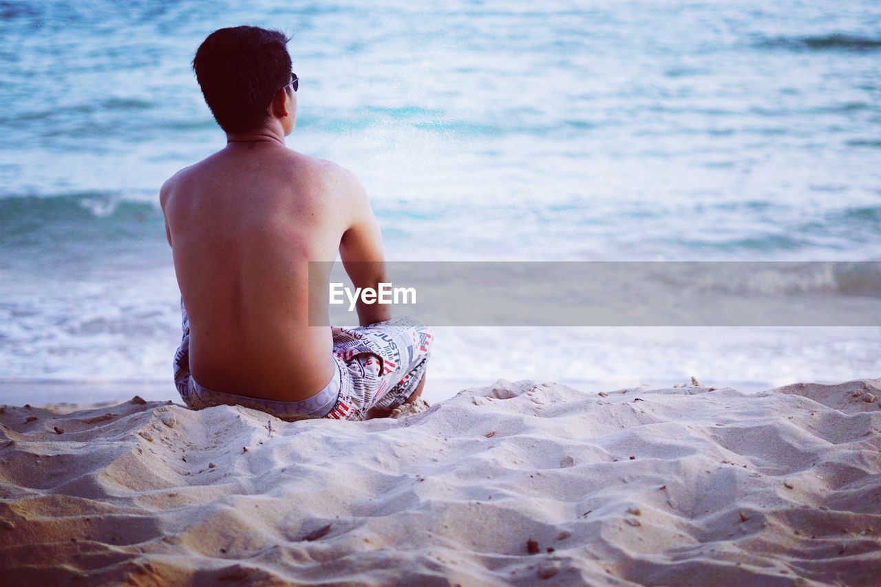 REAR VIEW OF SHIRTLESS MAN IN SEA AT BEACH