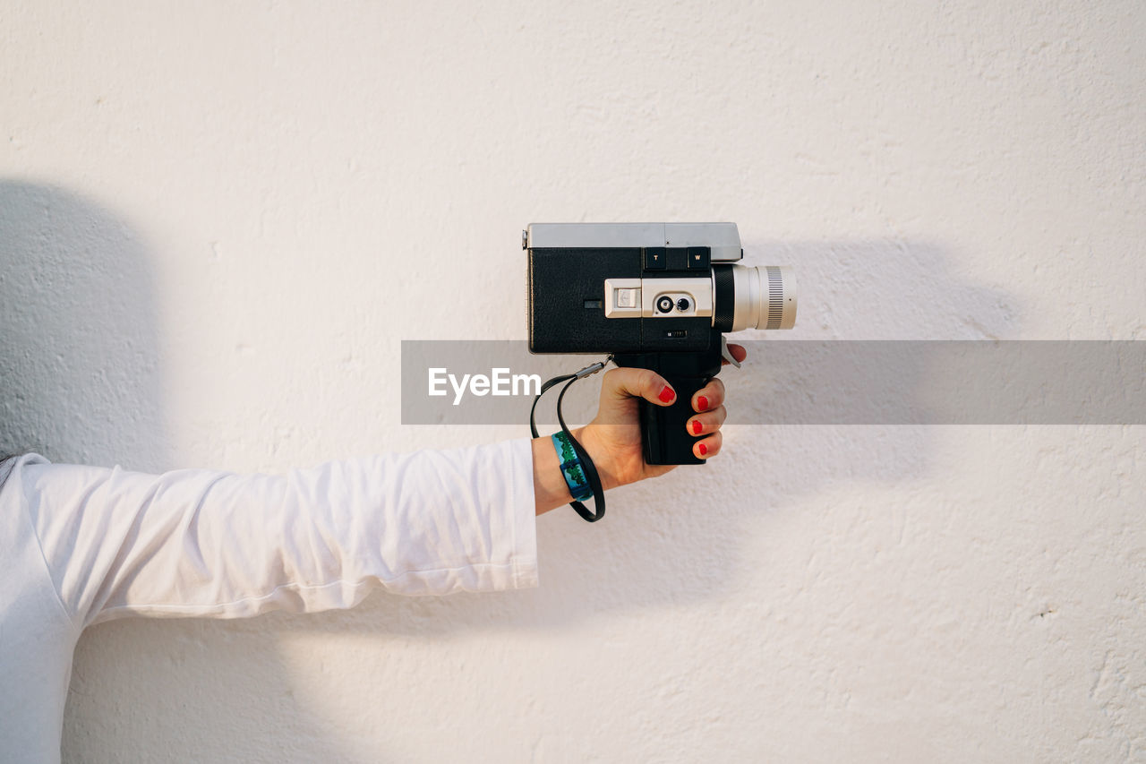 Hand holding camera against white wall