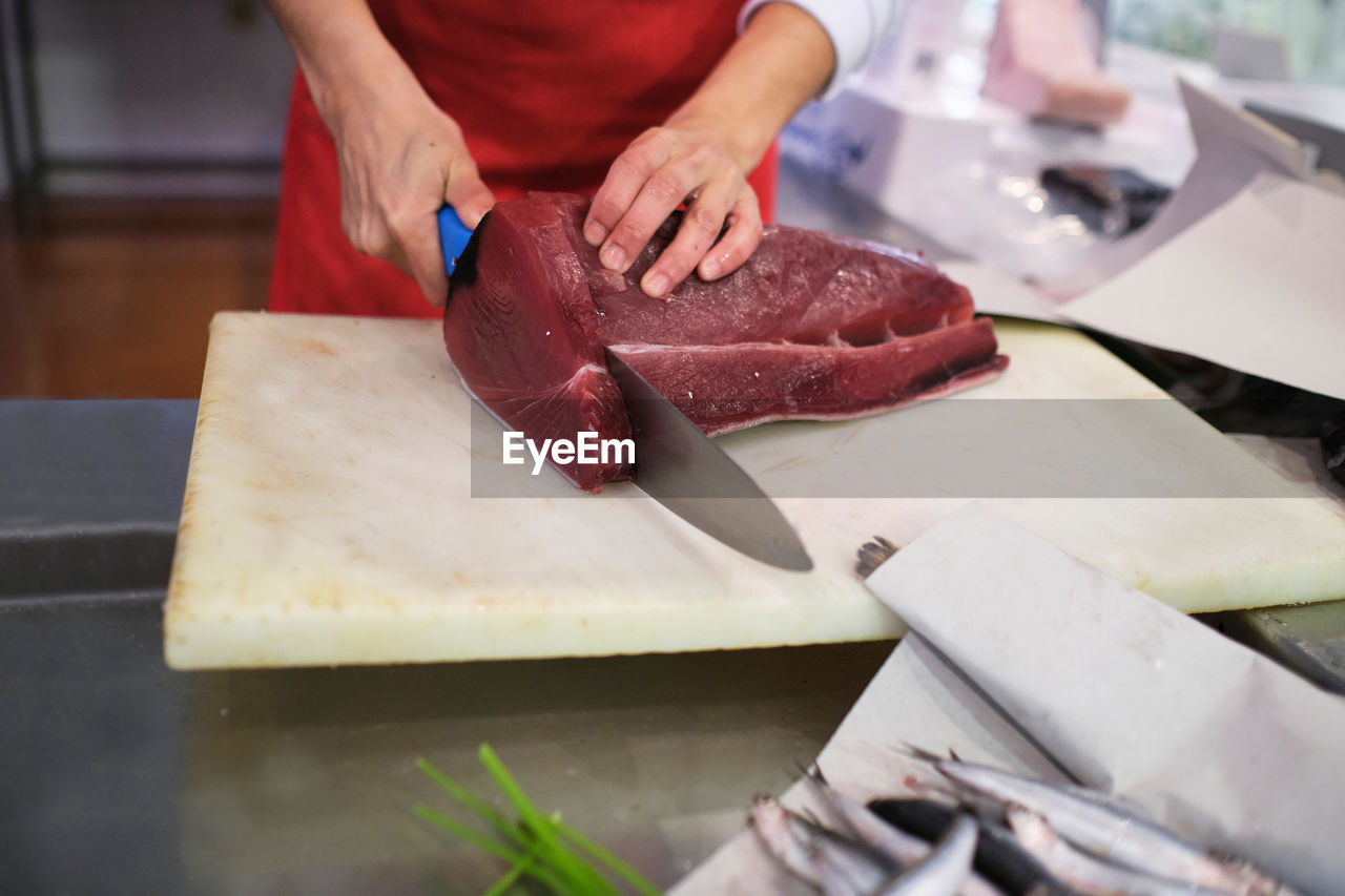 Young woman cuts up a red fish in her fishmonger's