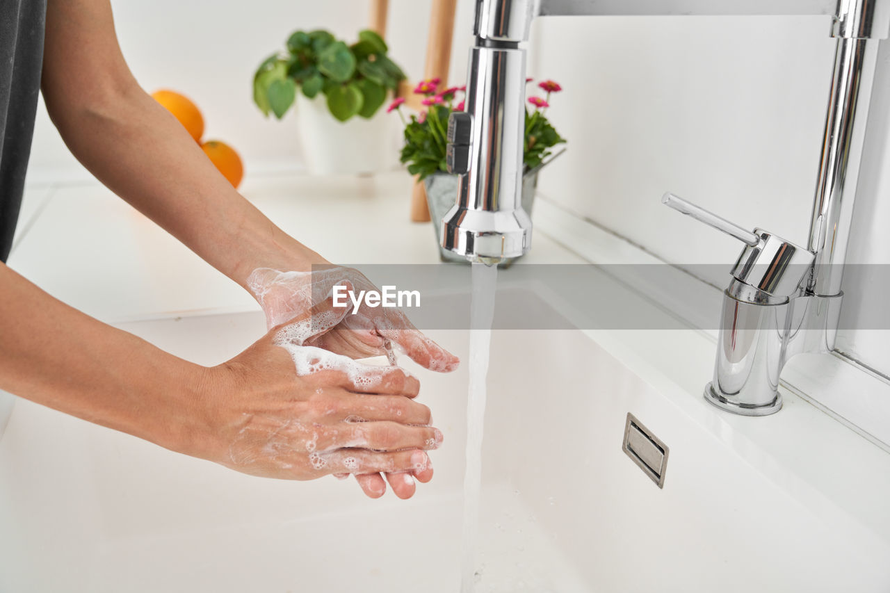 Woman washing her hands on the kitchen sink to avoid possible infection