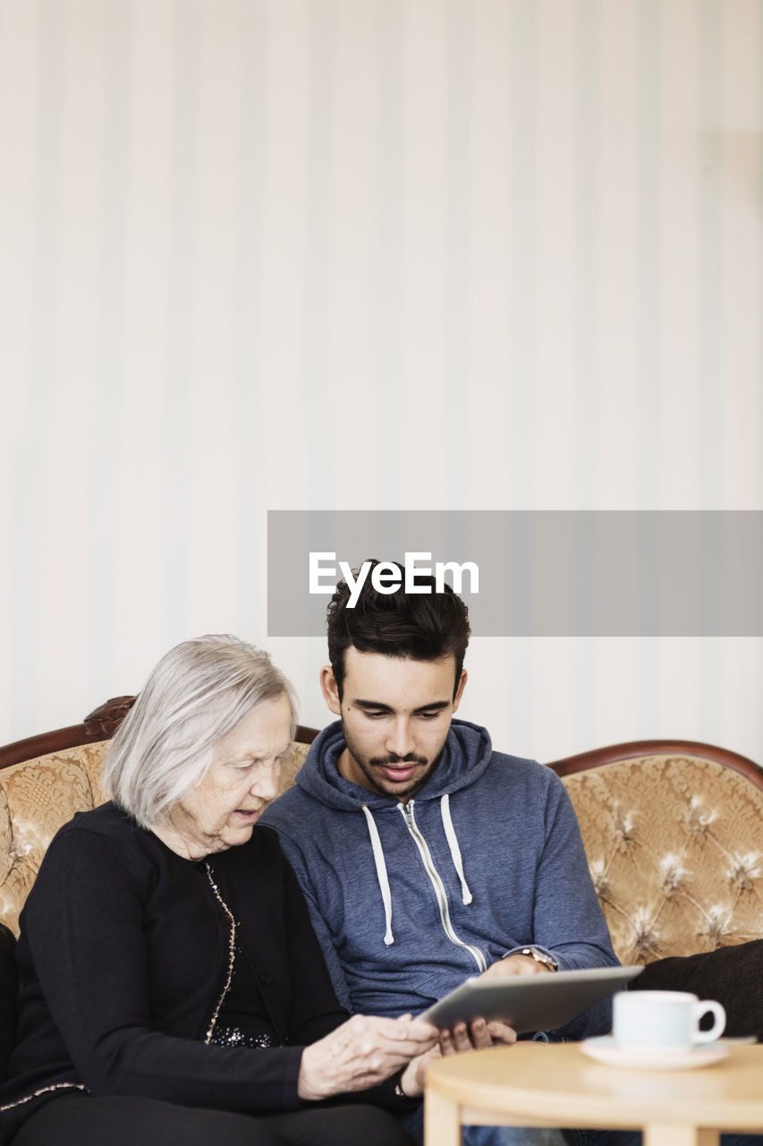 Caretaker and senior woman using digital tablet while sitting on sofa at nursing home