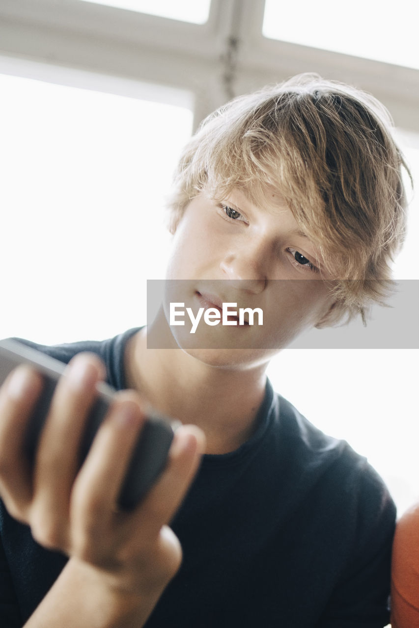Close-up of teenage boy using smart phone against window