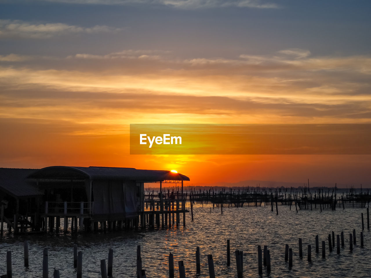 sky, sunset, water, sea, cloud, pier, architecture, beauty in nature, nature, built structure, beach, scenics - nature, tranquility, tranquil scene, orange color, land, wood, evening, horizon, hut, dusk, idyllic, building exterior, no people, ocean, stilt house, sun, wooden post, building, outdoors, travel destinations, horizon over water, post, sunlight, coast, reflection, silhouette, holiday, dramatic sky, shore, vacation, trip, tourism, travel, house, non-urban scene, afterglow