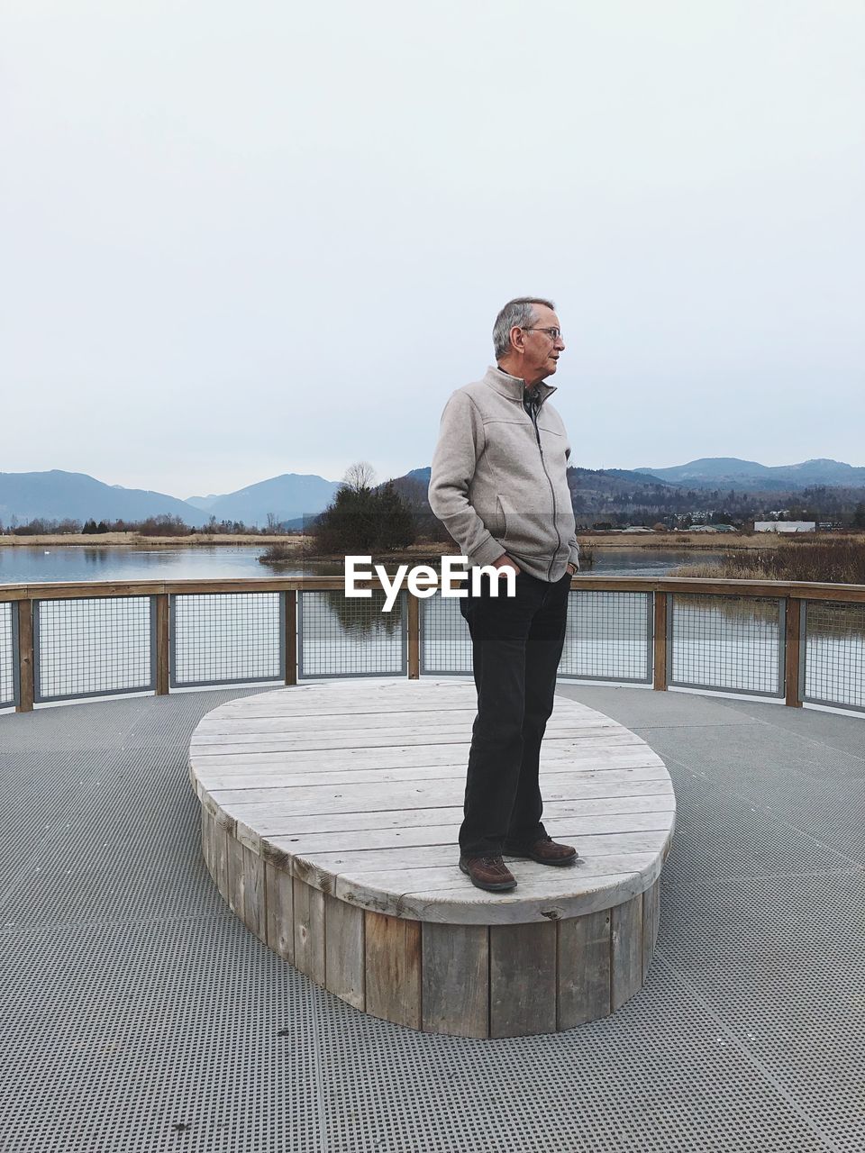 MAN STANDING ON RAILING AGAINST LAKE