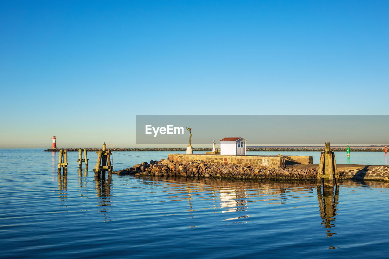 Pier on sea against clear blue sky