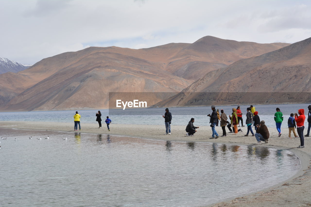 People at shore of pangong lake against mountains