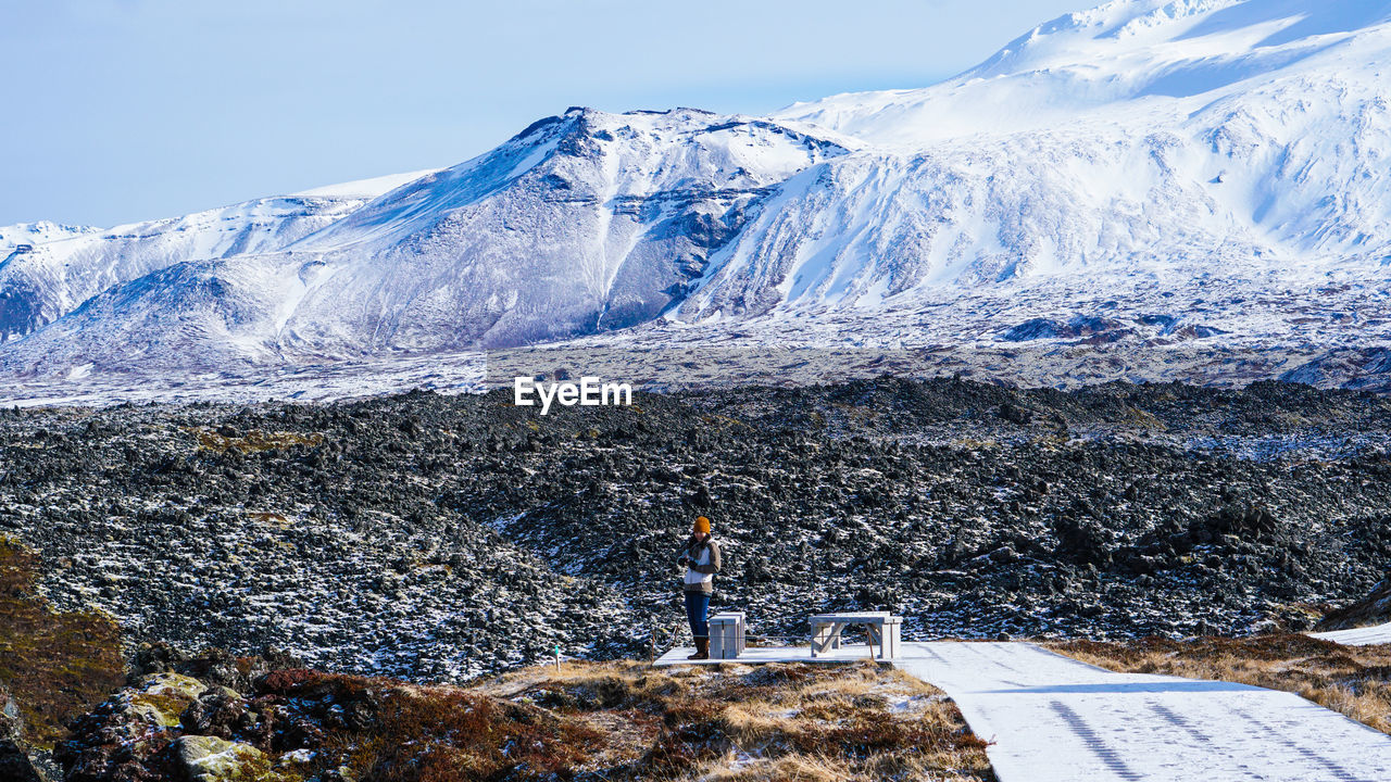 Woman standing on land against snowcapped mountain