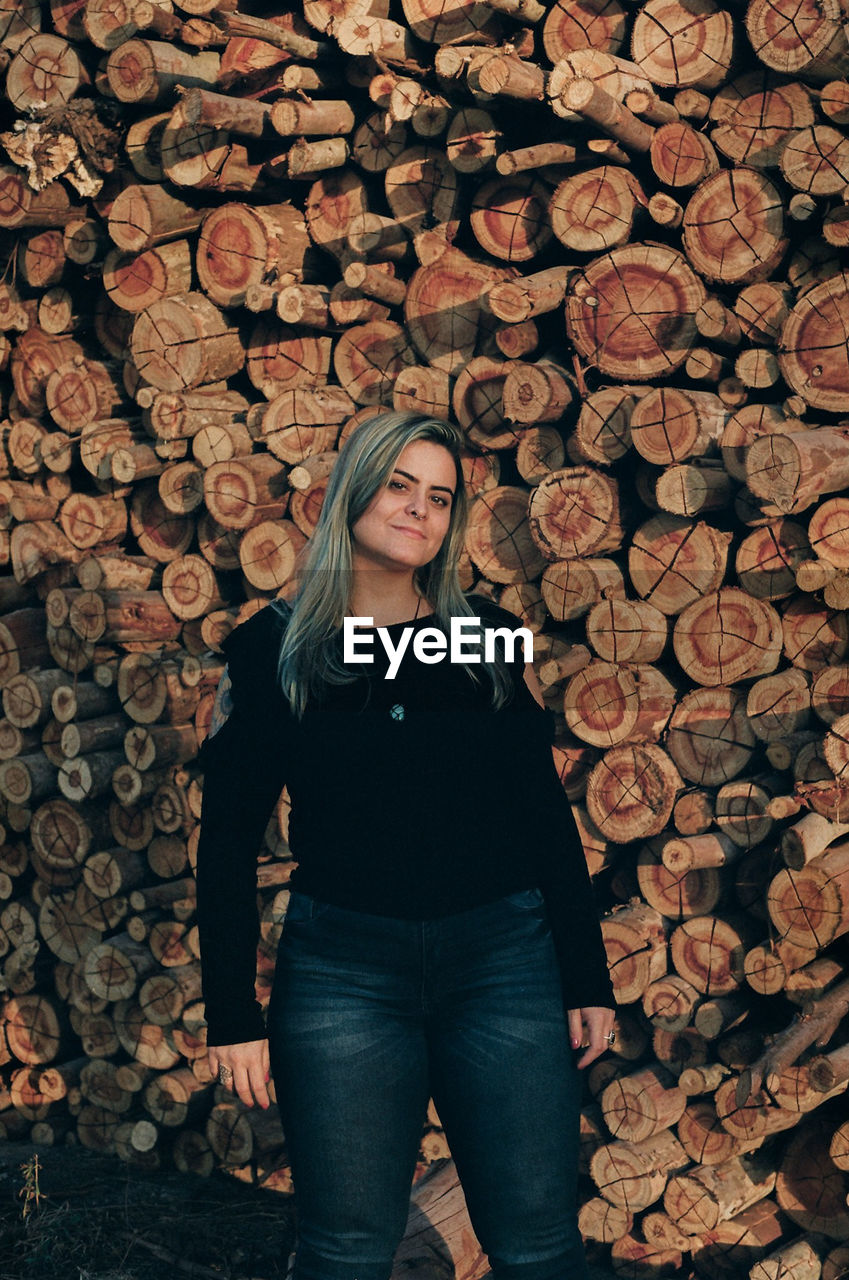 Portrait of woman standing against stacked logs