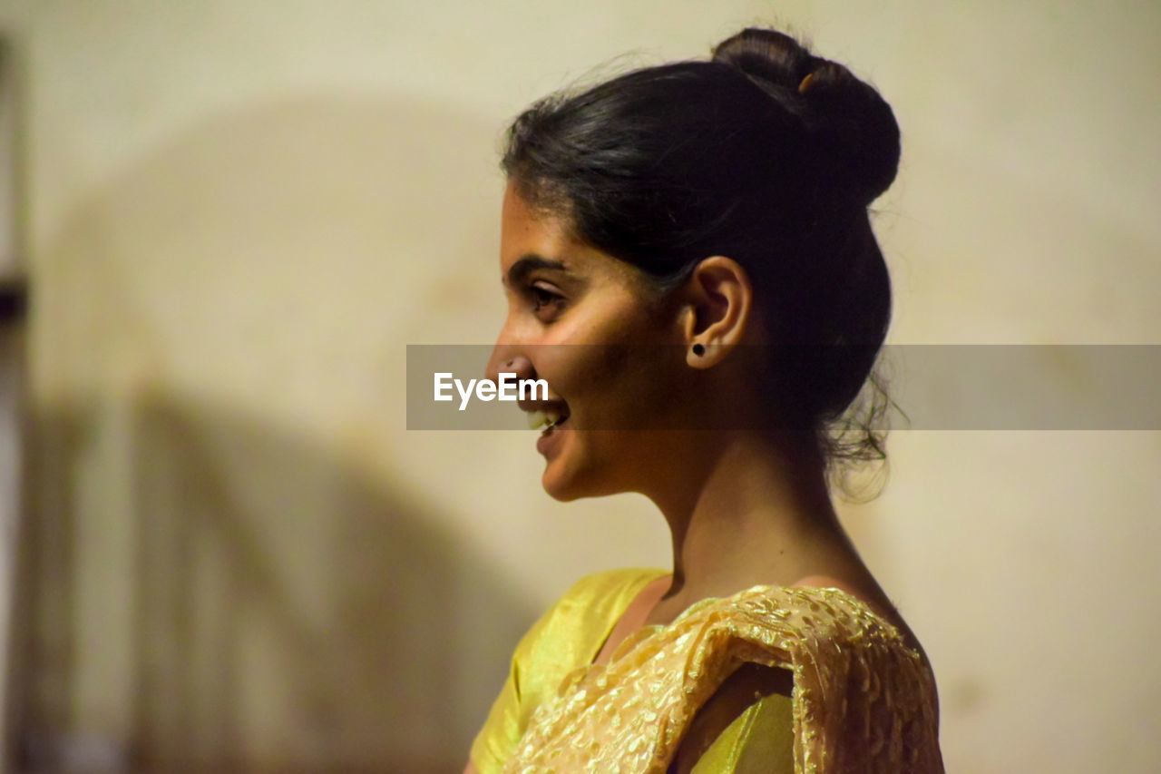 one person, adult, women, portrait, young adult, headshot, side view, looking, profile view, hairstyle, looking away, hair bun, bun, fashion, female, clothing, indoors, yellow, emotion, focus on foreground, jewelry, person, smiling, arts culture and entertainment, human face, earring, happiness, black hair, bride, lifestyles, human hair, elegance, copy space, photo shoot