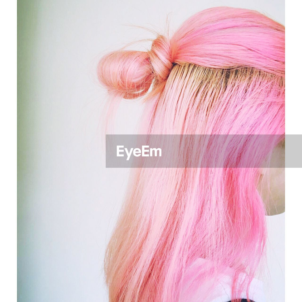 Side view of woman with pink dyed hairstyle standing against white wall