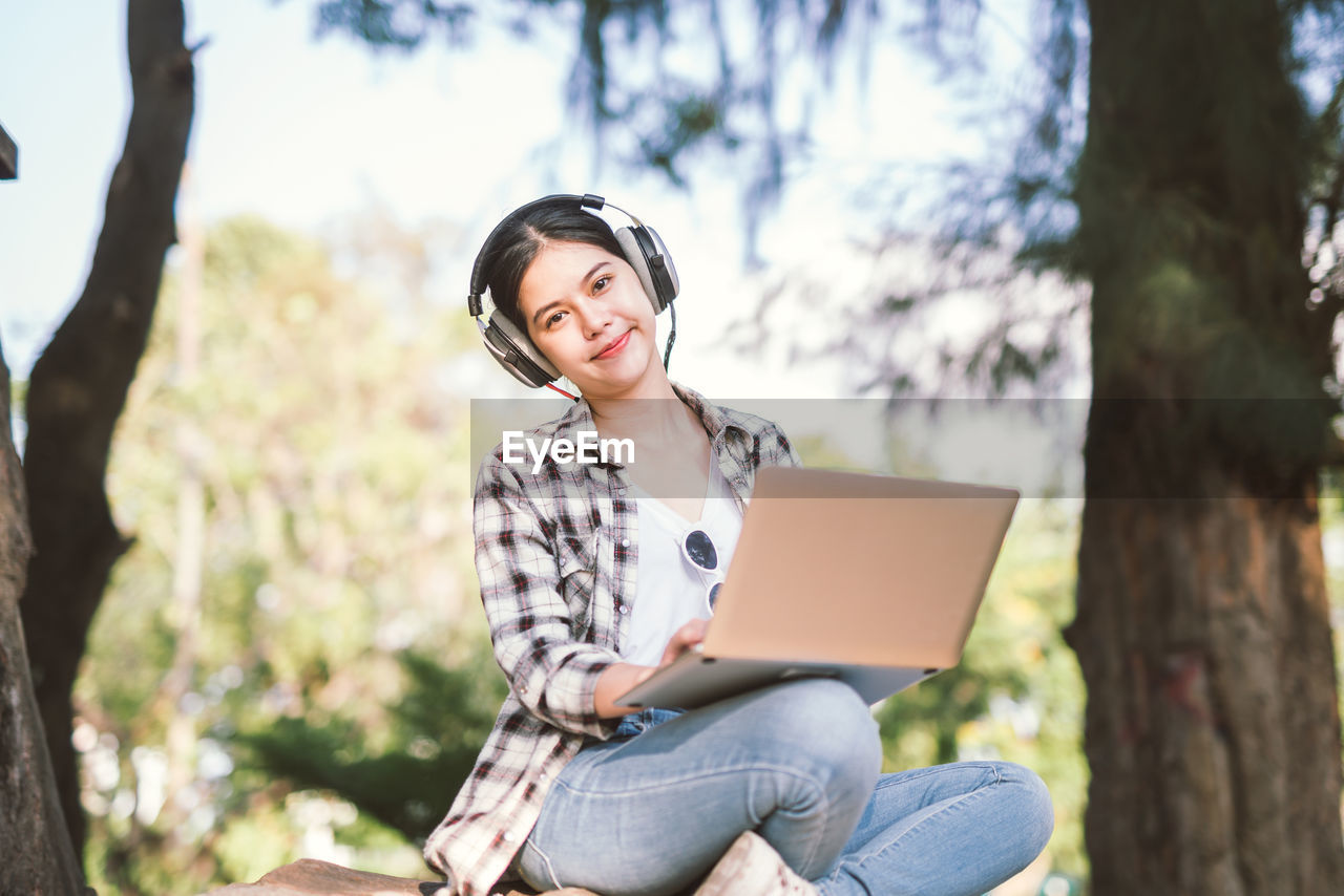 Portrait of young woman using laptop against trees