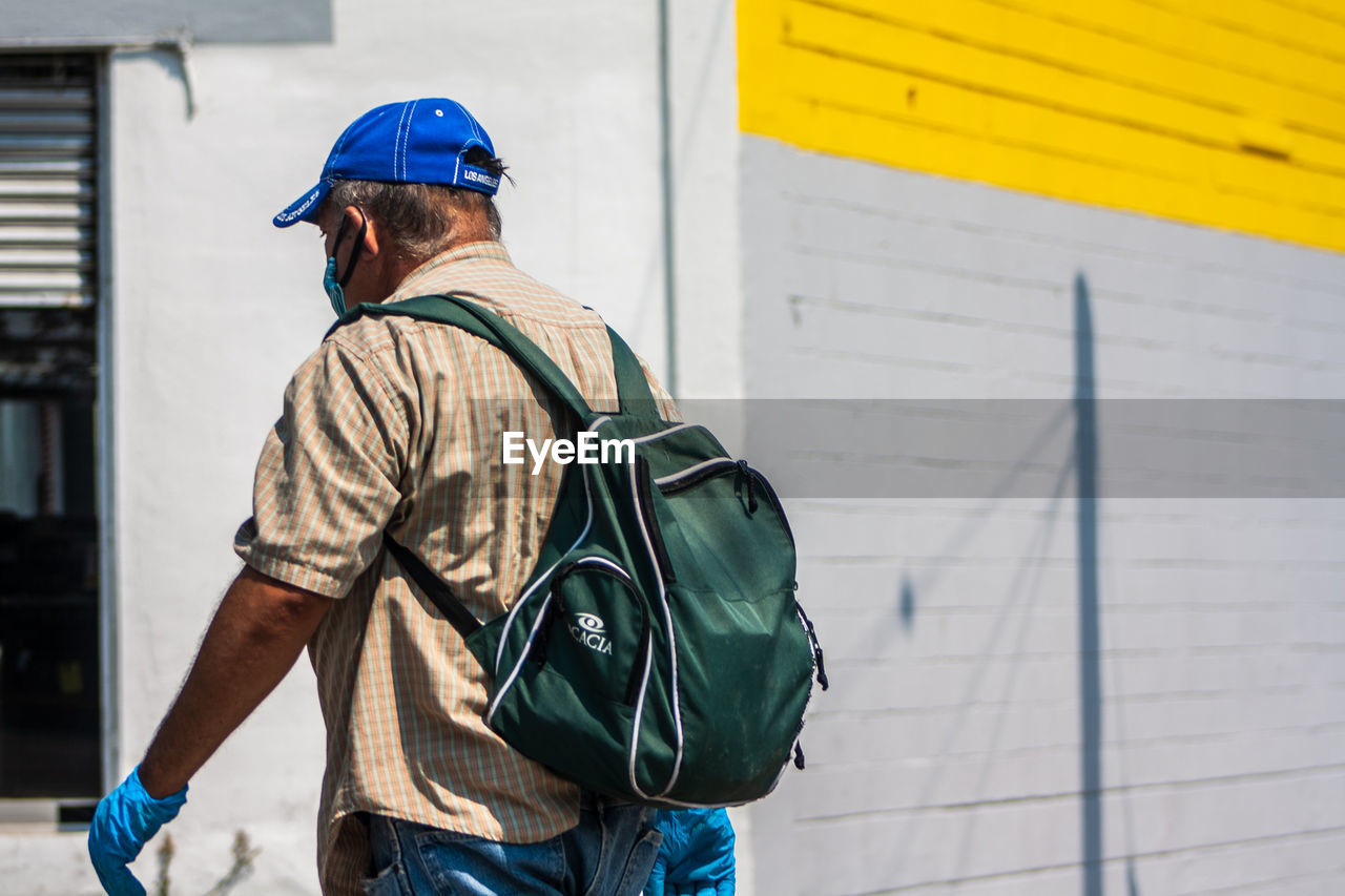 REAR VIEW OF MAN STANDING AGAINST BRICK WALL