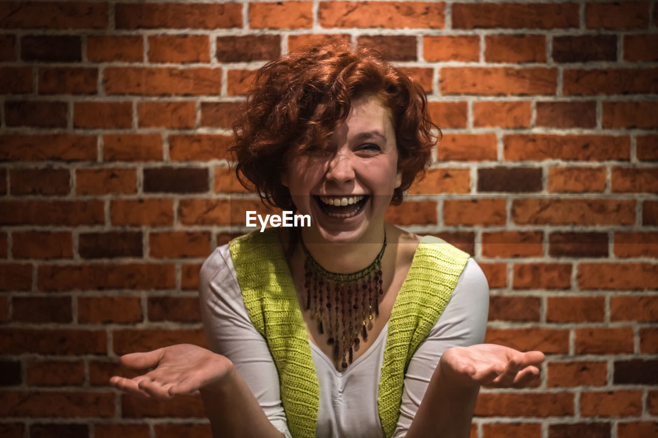 Portrait of cheerful young woman against brick wall